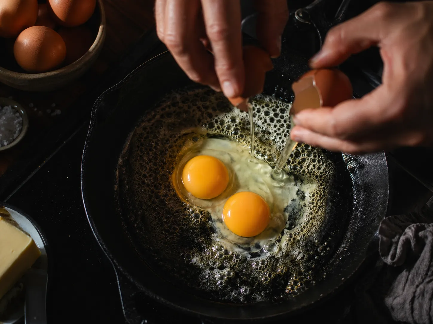 Eggs cracking into a cast iron skillet