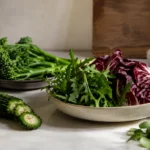 Bitter foods including arugula, radicchio, broccoli rabe, watercress, and bitter melon arranged on a neutral kitchen surface, illustrating the connection between bitter foods and GLP-1.