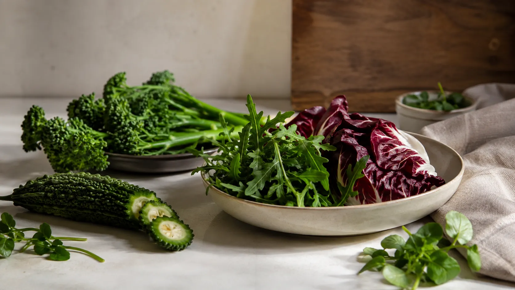 Bitter foods including arugula, radicchio, broccoli rabe, watercress, and bitter melon arranged on a neutral kitchen surface, illustrating the connection between bitter foods and GLP-1.