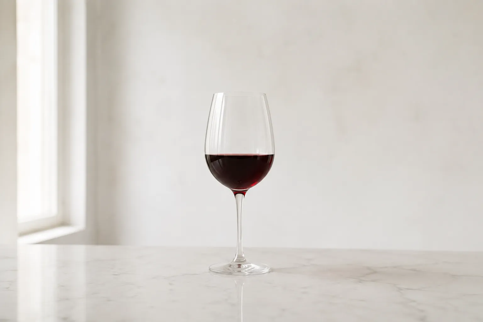 A single glass of red wine on a pale counter in daylight